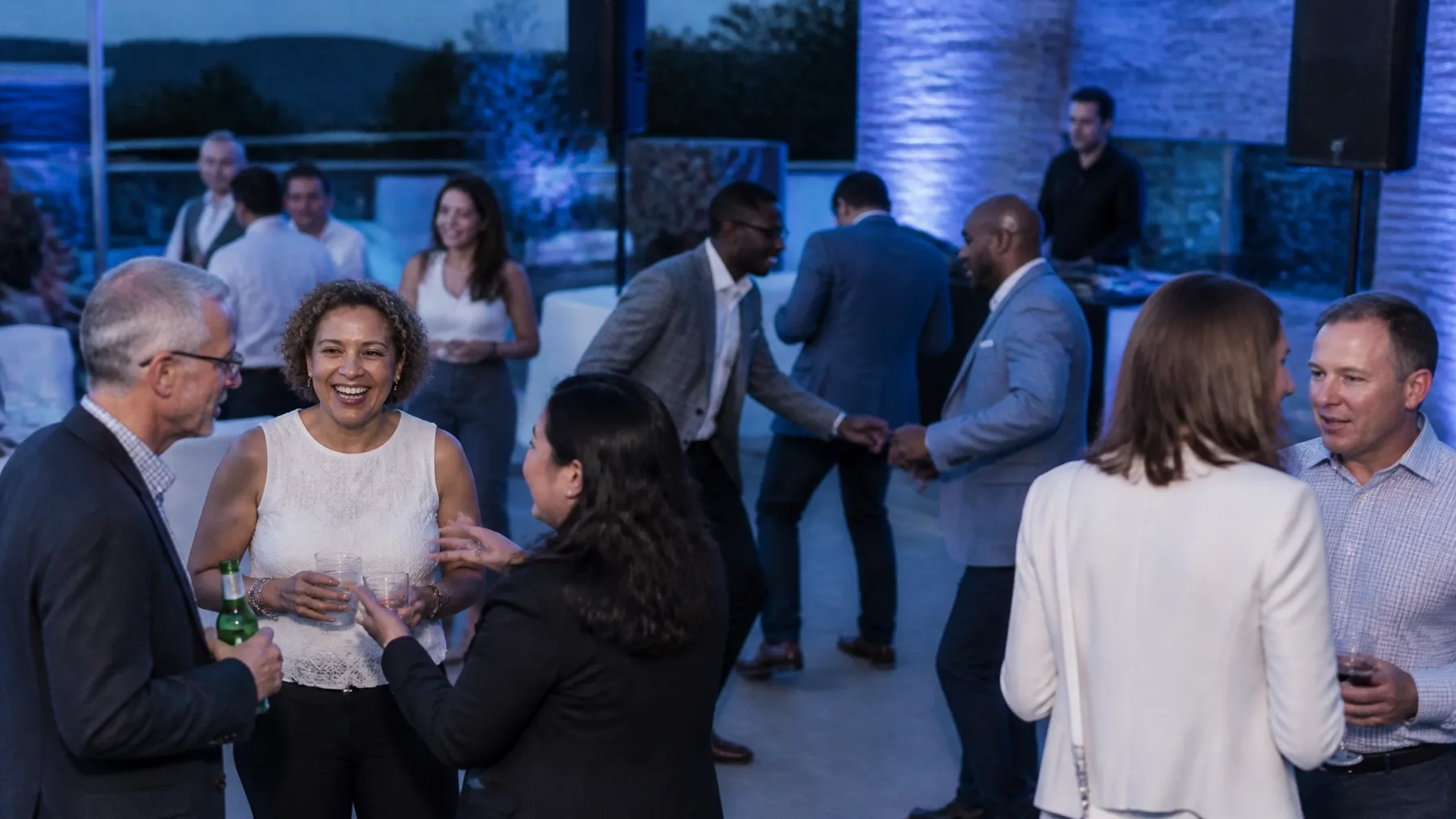 Professional adults networking and dancing at a polished corporate celebration with a DJ system visible behind them