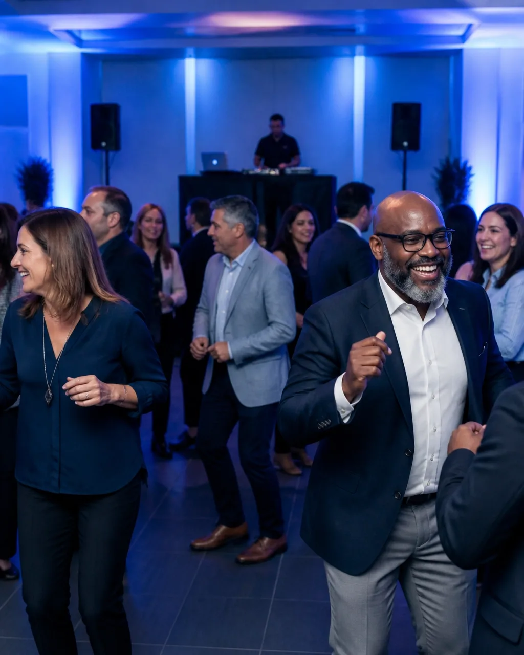 Diverse adult coworkers dancing and smiling at an employee celebration with a DJ system behind them